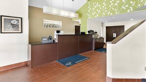 A reception area with a brown counter, a black mat, and a green wall with white patterns. - Sleep Inn & Suites Princeton I-77 (Princeton)