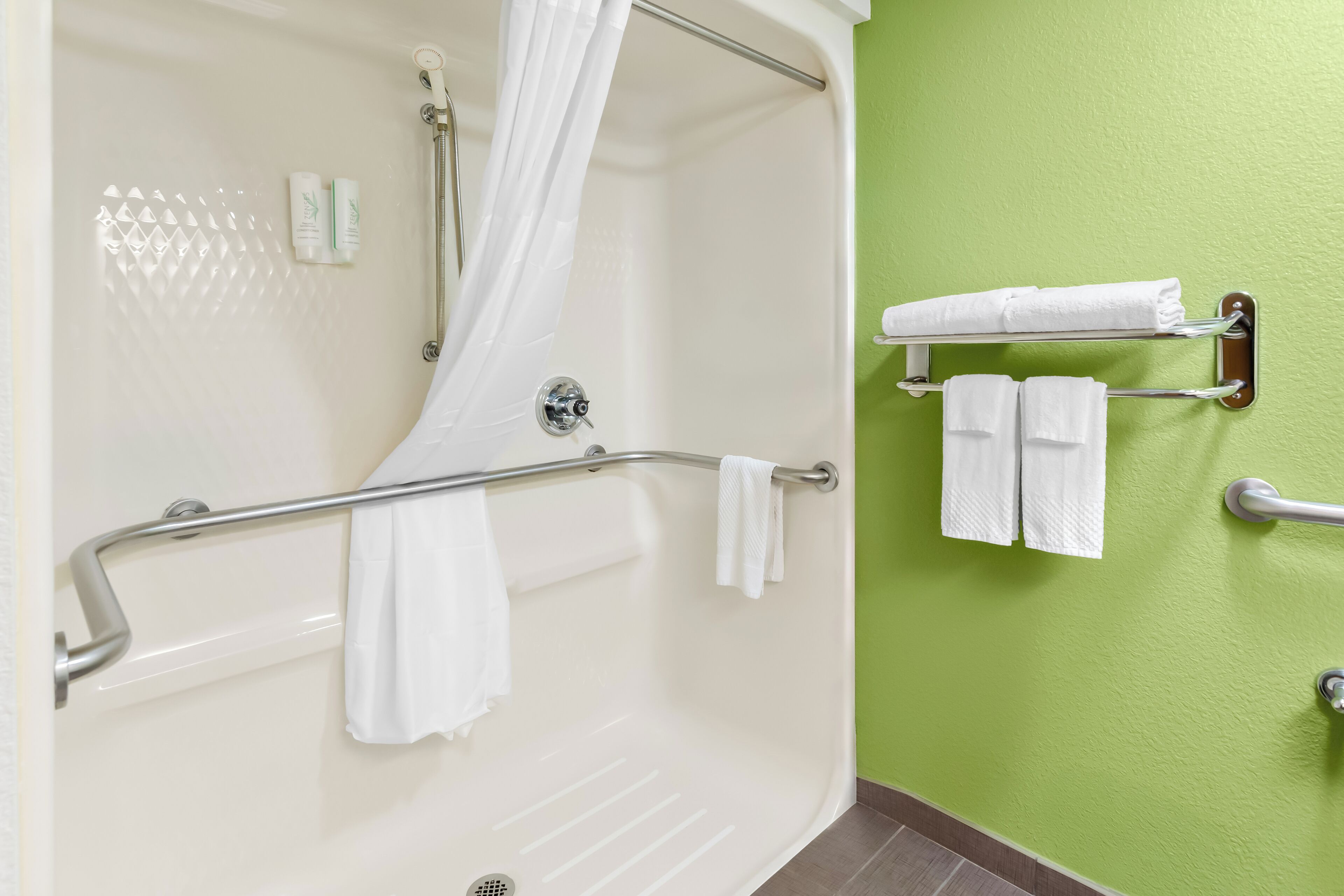 A bathroom with a shower, a towel rack, and a green wall.