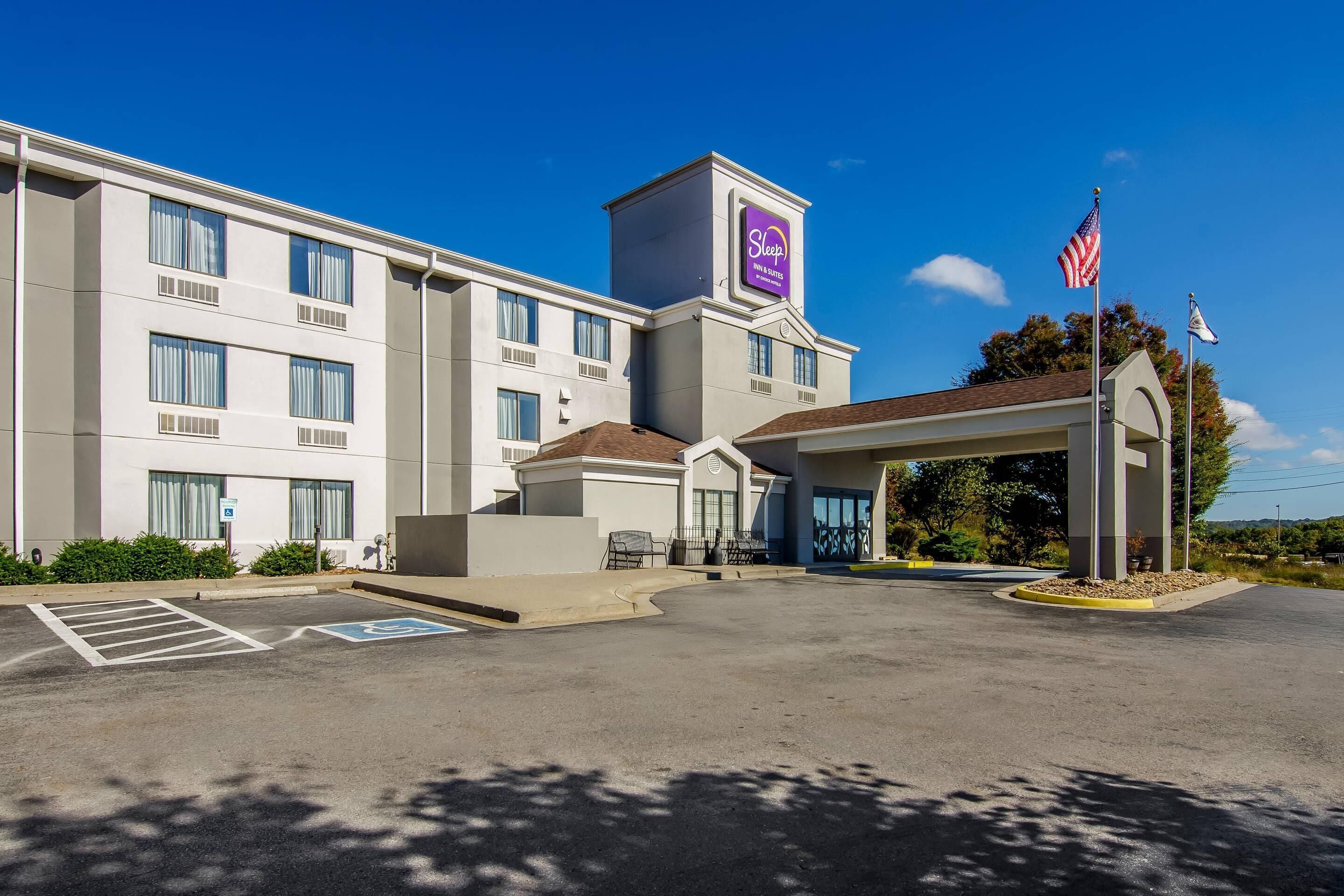 Un hotel moderno con entrada central, estacionamiento y la bandera estadounidense.