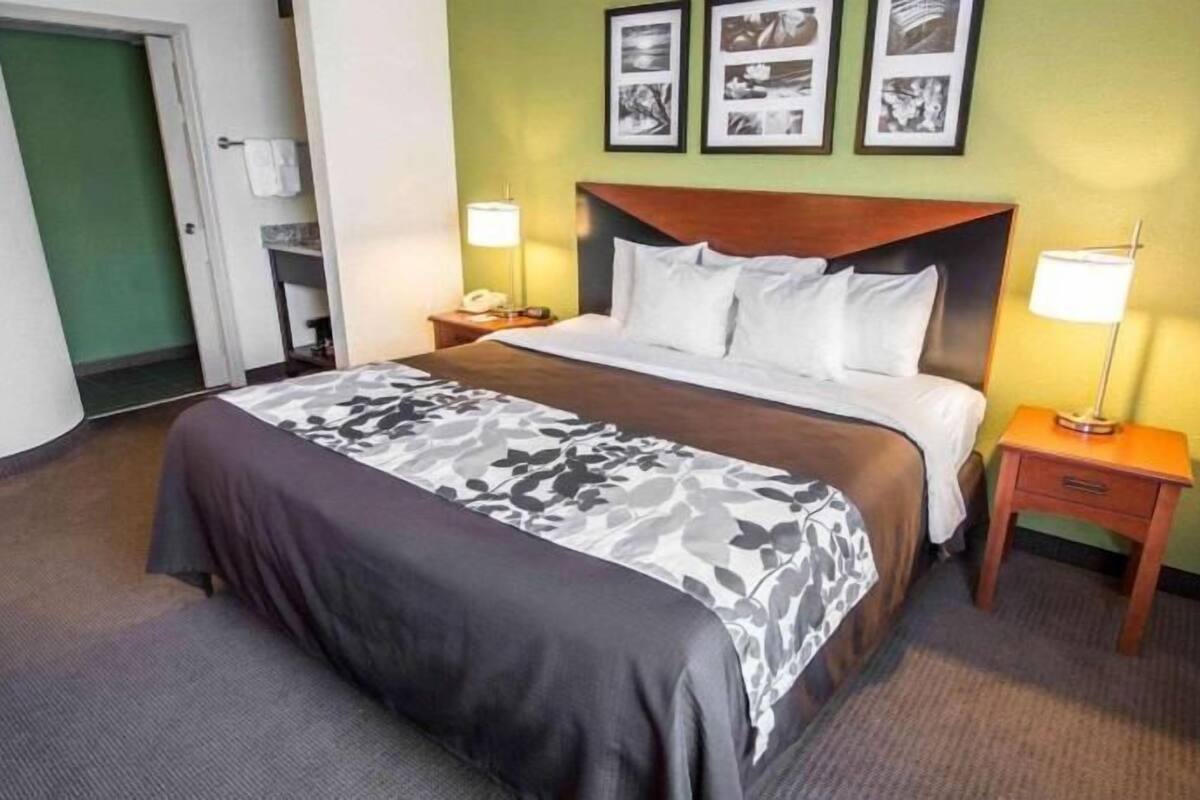 A hotel room with a bed, two bedside tables, a nightstand, a door, and a wall with framed pictures.
