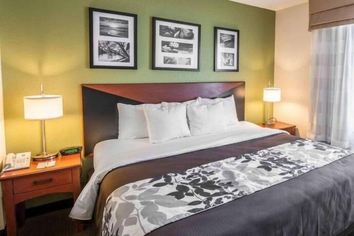 A hotel room with a bed, two bedside tables, a lamp, a clock, and framed pictures on the wall.