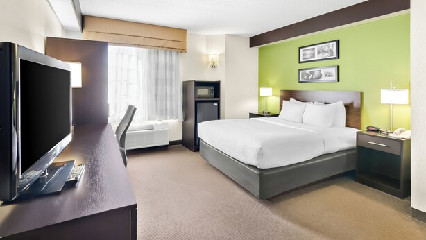 A hotel room with a bed, a desk with a TV, a desk lamp, a nightstand with a phone, and a window with curtains. - Sleep Inn & Suites Princeton I-77 (Princeton)