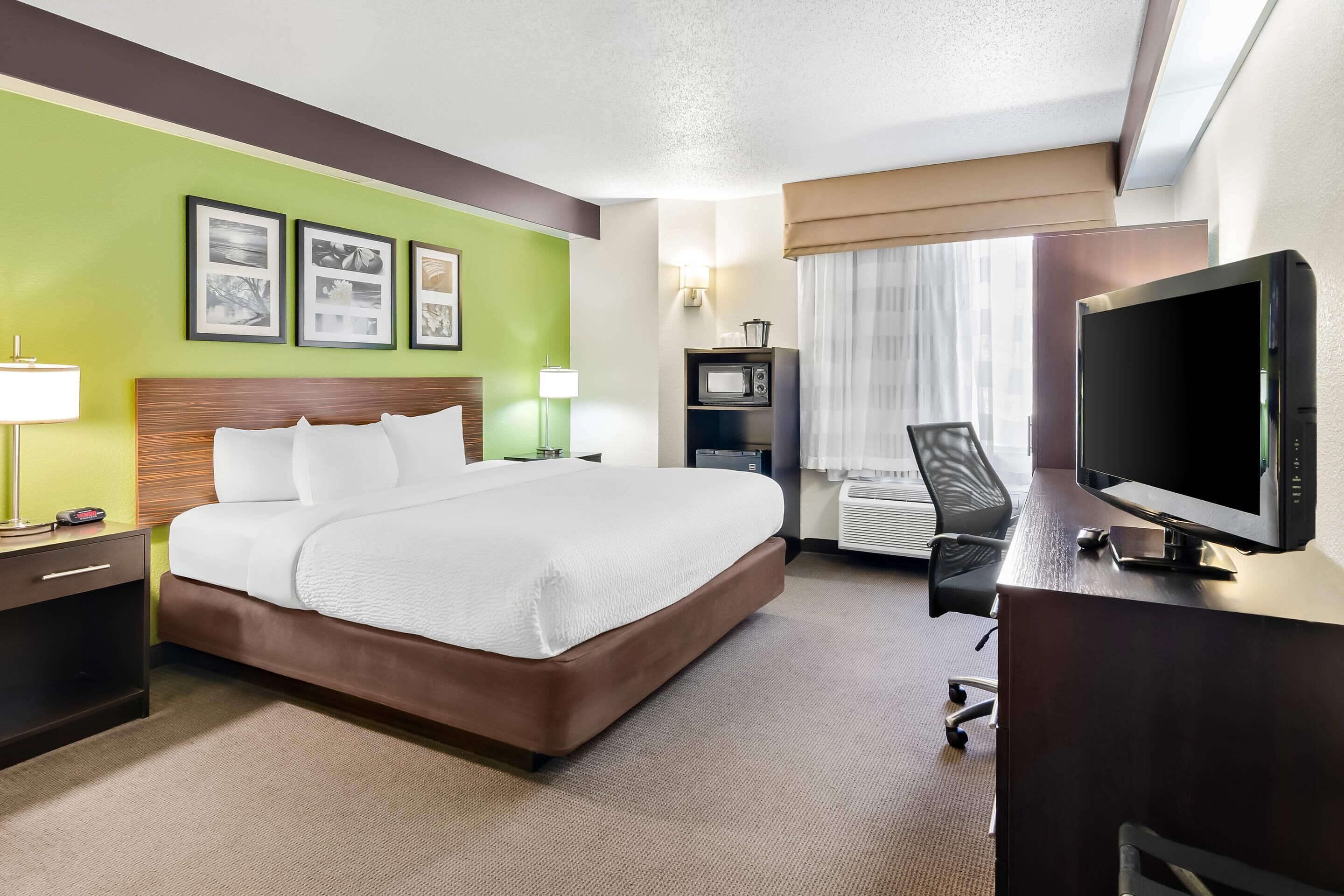 A hotel room with a bed, a desk with a TV, a microwave, and a chair.