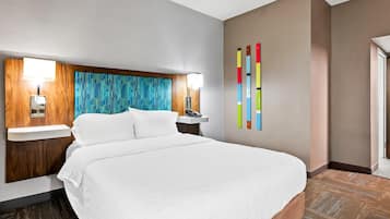 Een hotelkamer met een groot bed, een houten hoofdbord, een nachtkastje met lamp en een kleurrijk abstract kunstwerk aan de muur.