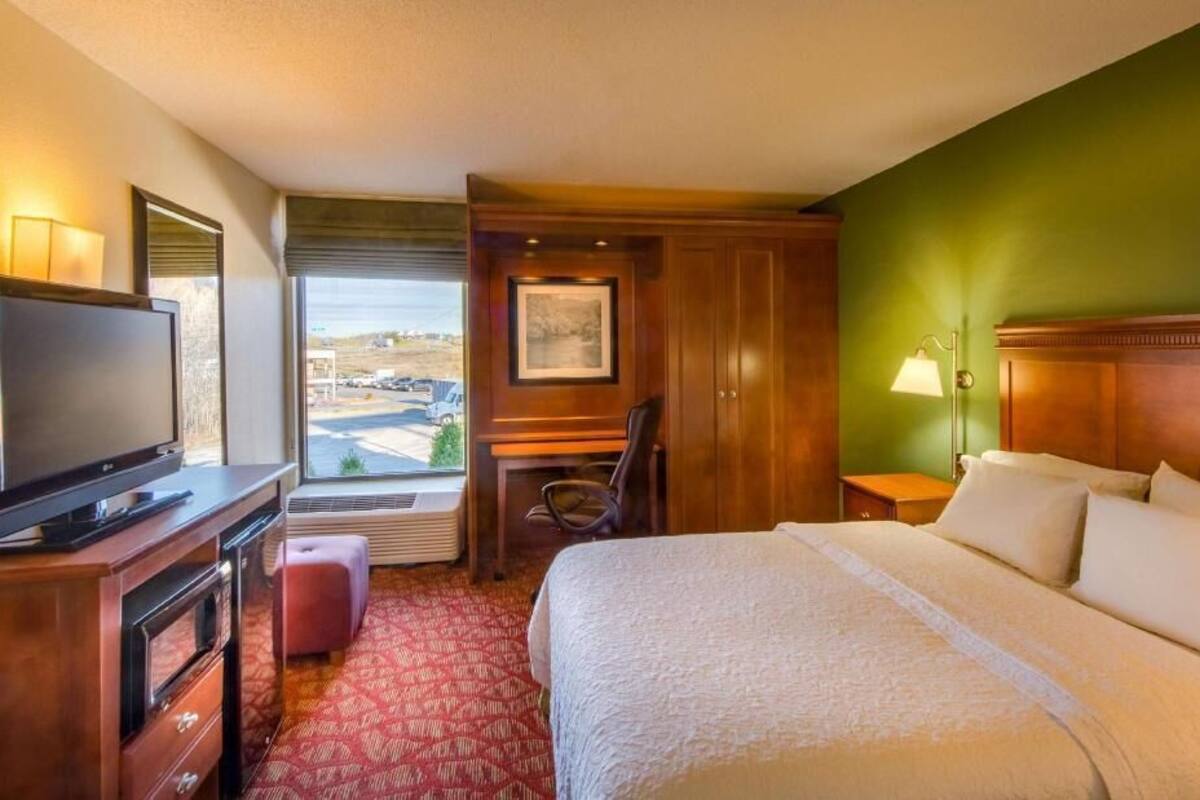 Ein Hotelzimmer mit Bett, Schreibtisch, Stuhl, Fernseher, Lampe und einem Fenster mit Aussicht.