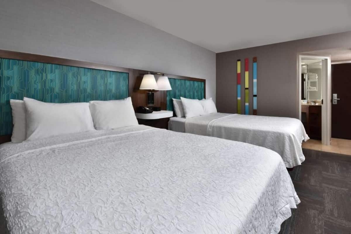Ein Hotelzimmer mit zwei Betten, einem Nachttisch, einer Lampe und einem Spiegel.