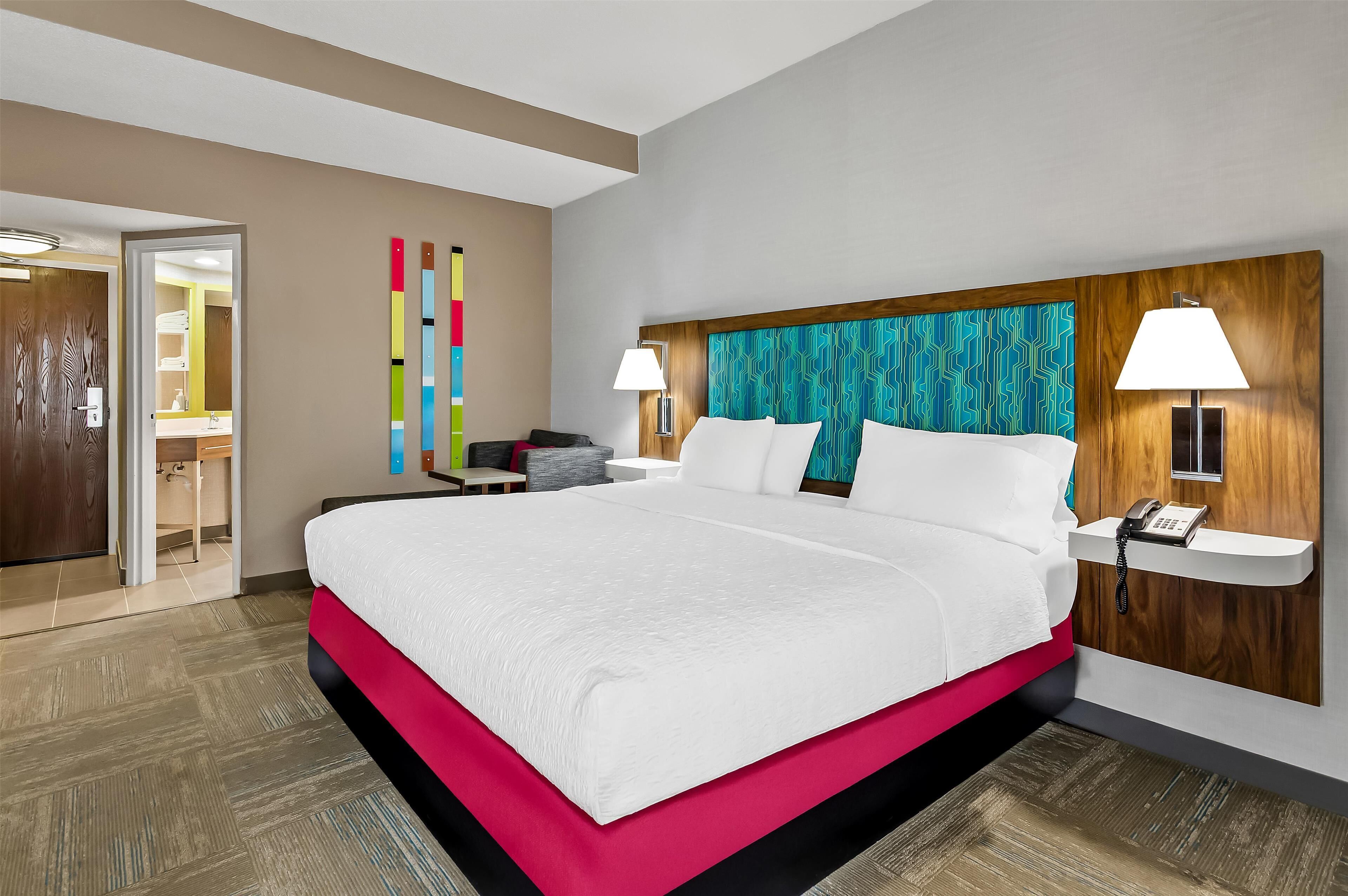 A hotel room with a large bed, a wooden headboard, a bedside table with a lamp, and a phone.