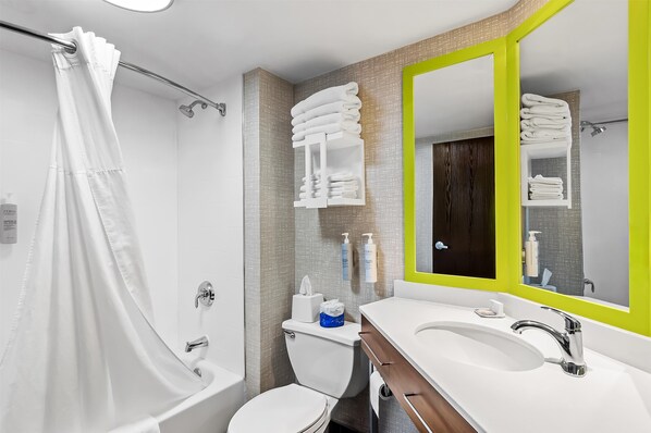 A modern bathroom with a shower, toilet, sink, and a mirror with a green frame.
