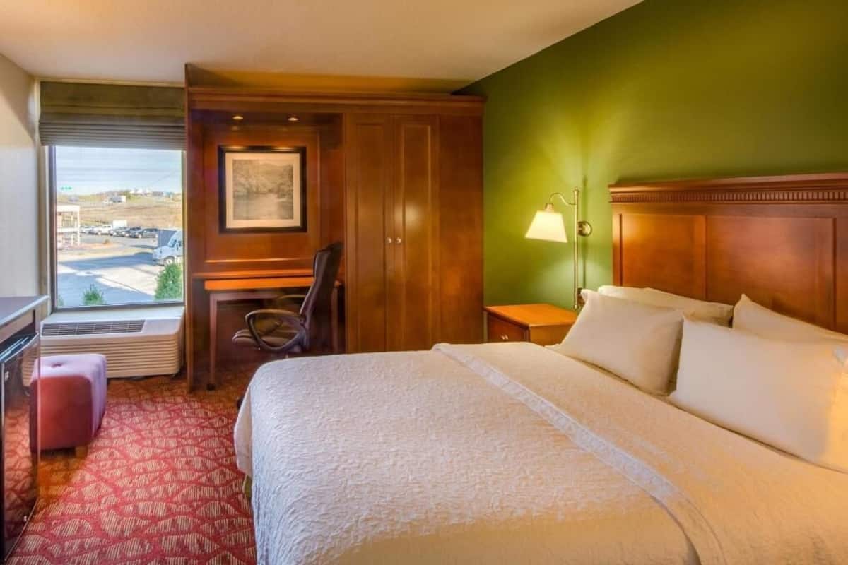 A hotel room with a bed, a desk, a chair, a lamp, and a window with a view.