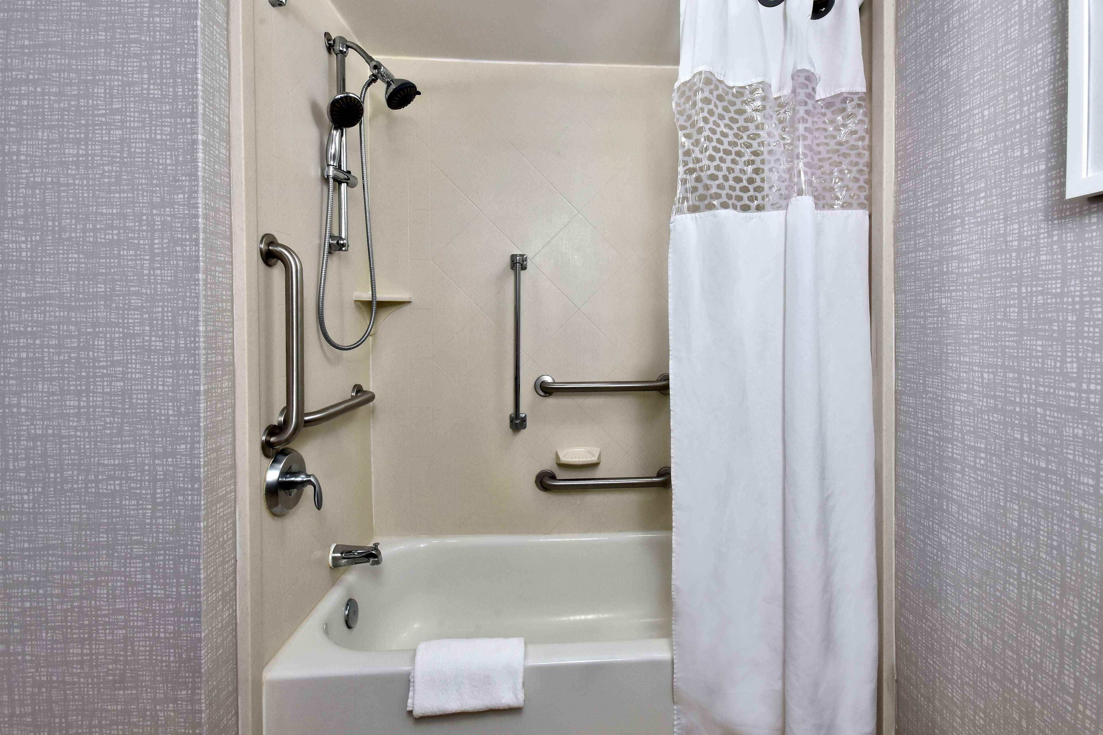 A bathroom with a bathtub, shower, grab bars, and a towel rack.