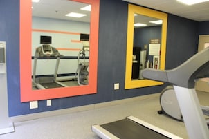 Un gimnasio con equipo de ejercicio, incluyendo cintas de correr y una bicicleta estática, y espejos en las paredes.