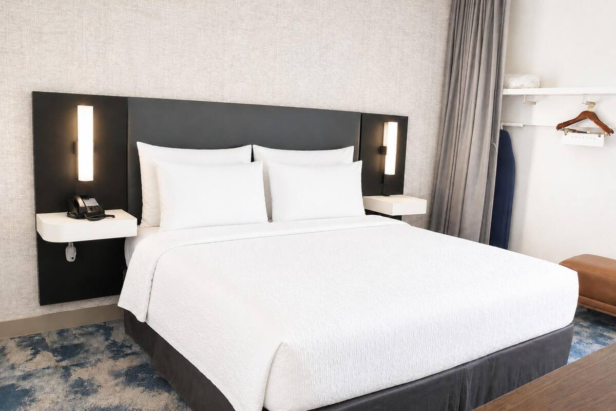 A hotel room with a large bed, bedside tables, a phone, and a hanging garment rack.