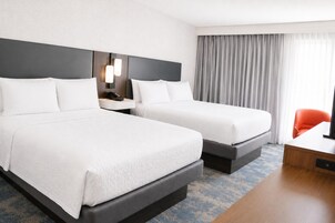 A hotel room with two beds, a desk, a chair, and a large window with curtains.