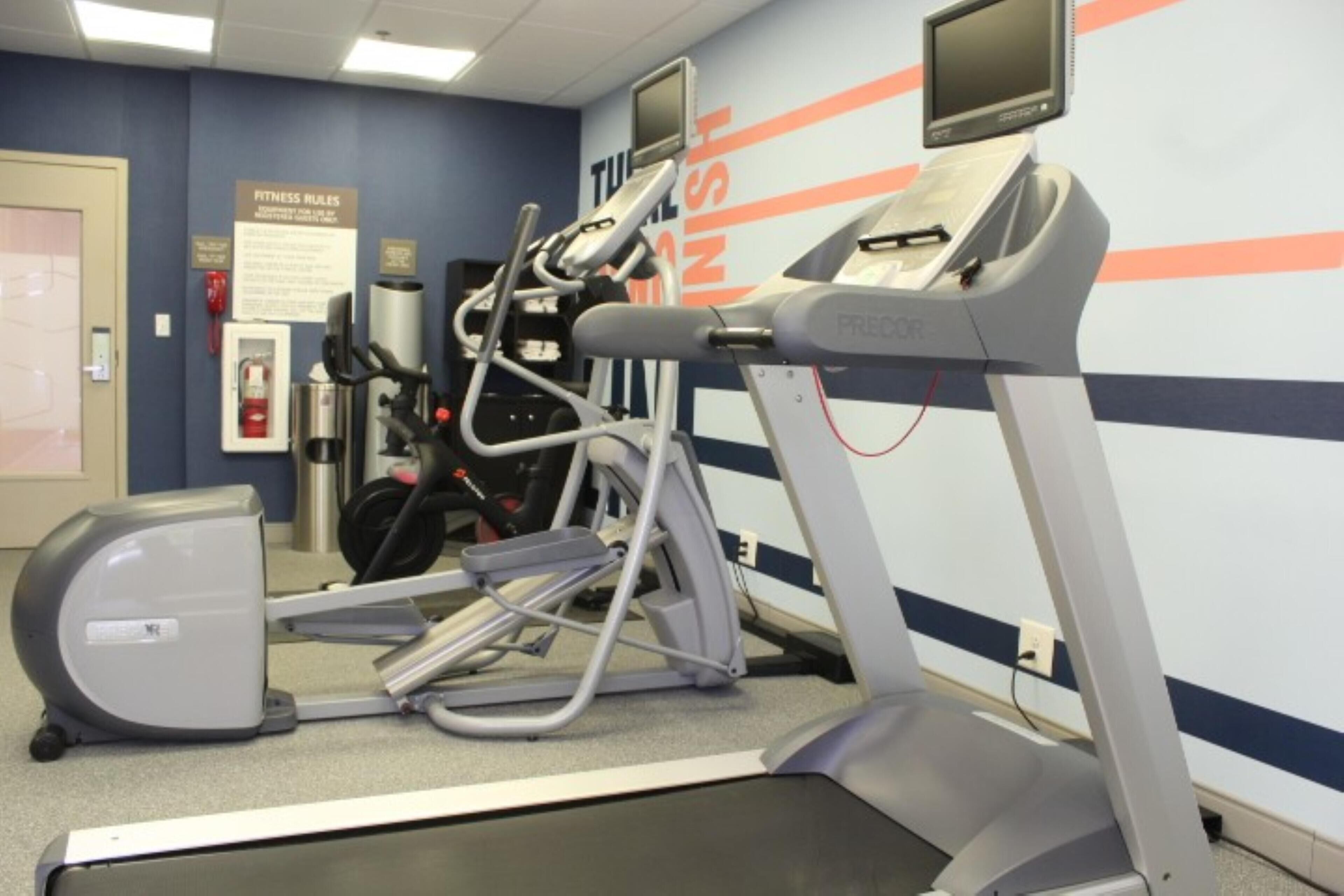 Une salle de sport équipée de tapis de course, de vélos elliptiques et d’appareils de musculation.