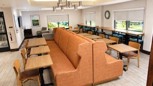 A modern dining area with a long orange sofa, wooden tables, and chairs. - Hampton Inn Summersville (Summersville)