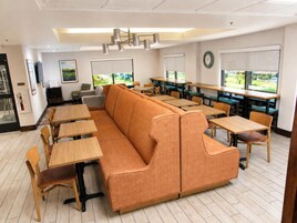A modern dining area with a long orange sofa, wooden tables, and chairs.