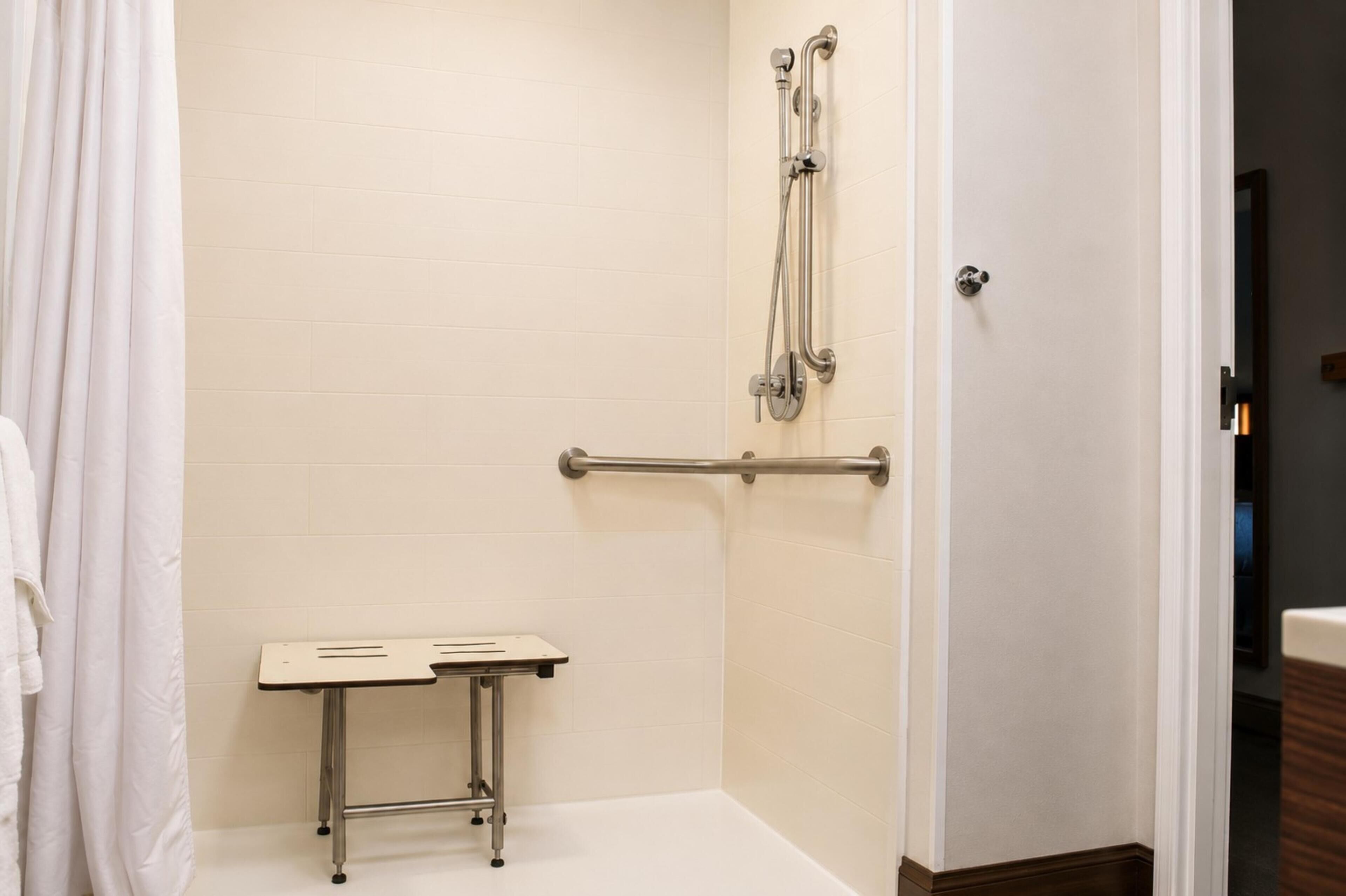 A bathroom with a shower, grab bars, a bench, and a door.