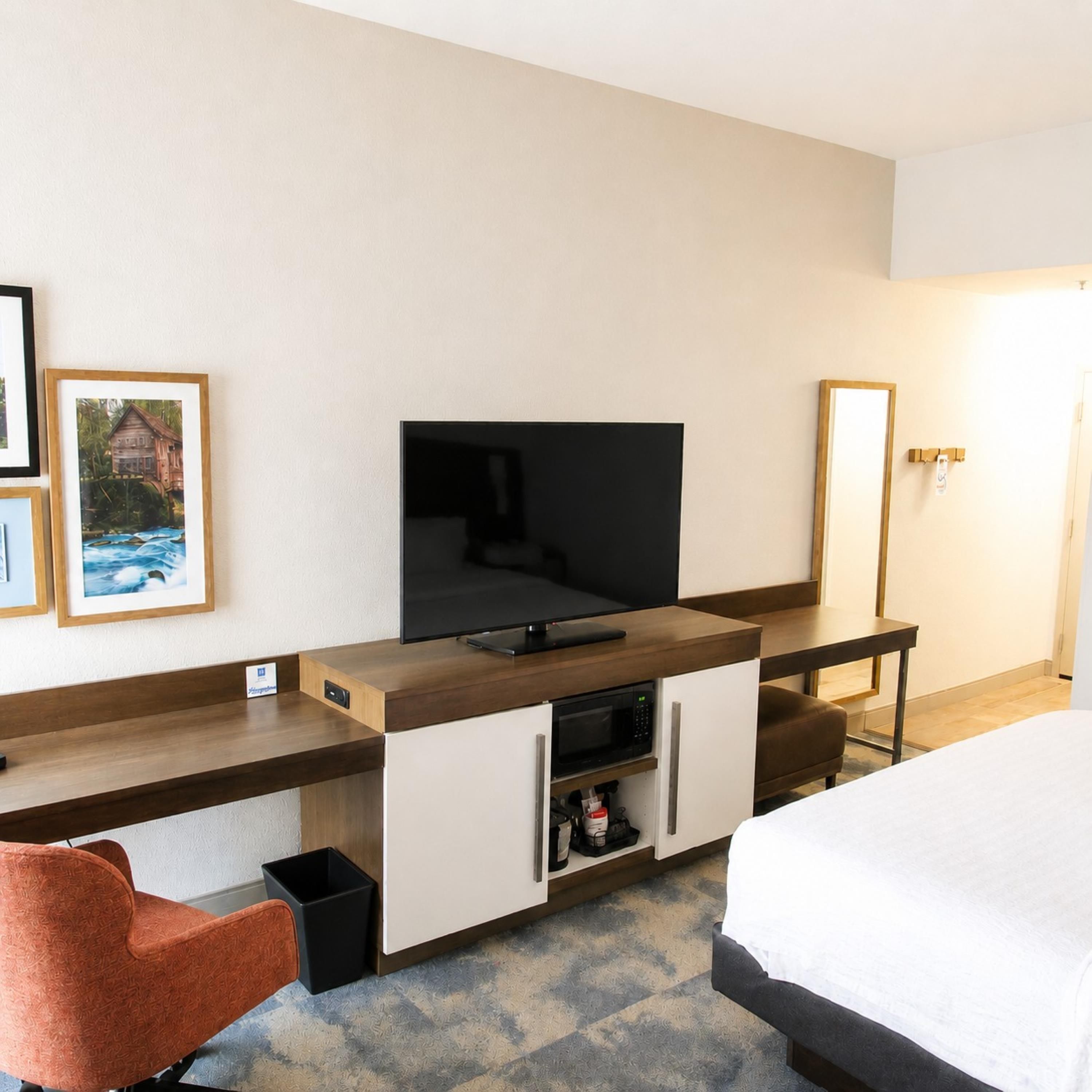 Une chambre d’hôtel comprenant un lit, un bureau avec une télévision, une chaise, un four à micro-ondes et un petit placard.