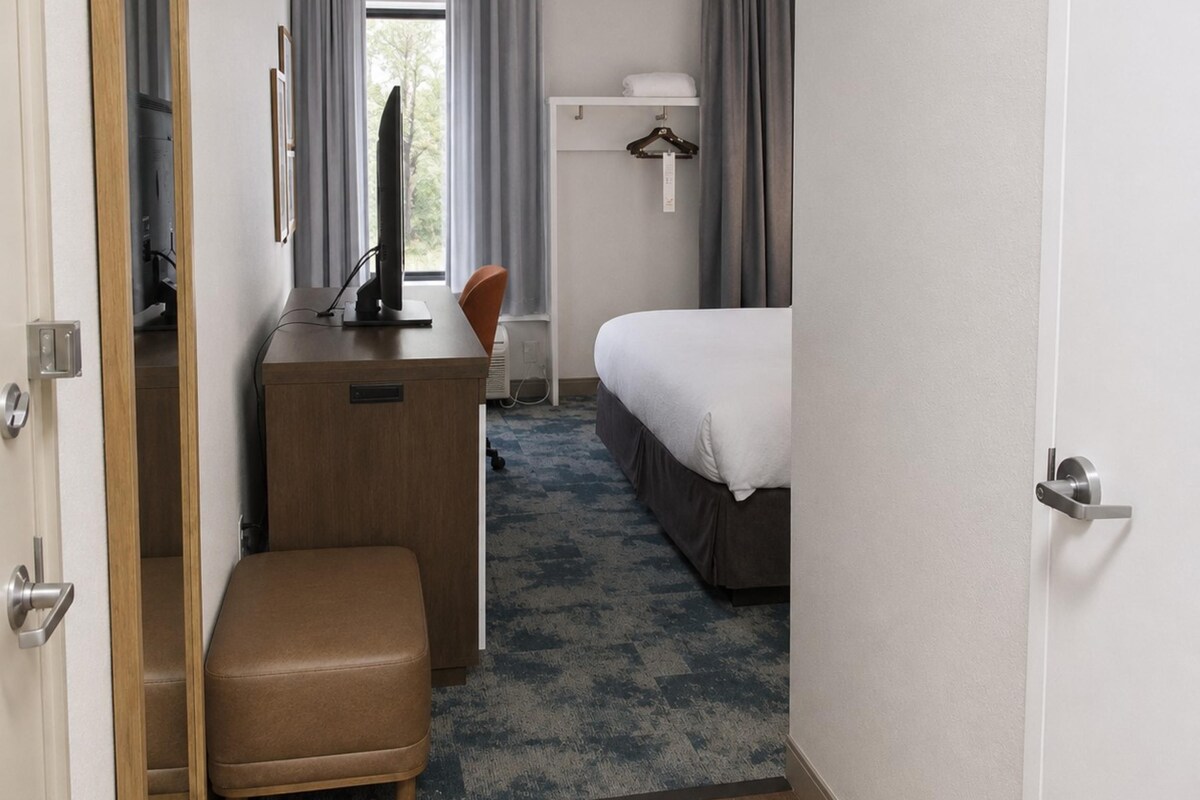 A hotel room with a desk, a bed, a TV, a wardrobe, and a bathroom visible through a door.