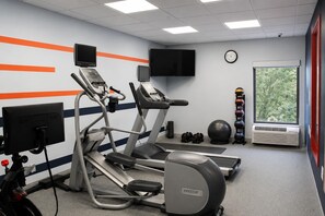 A gym with treadmills, a stationary bike, a rowing machine, a wall-mounted TV, a clock, a window with a view of trees, and a set of dumbbells.