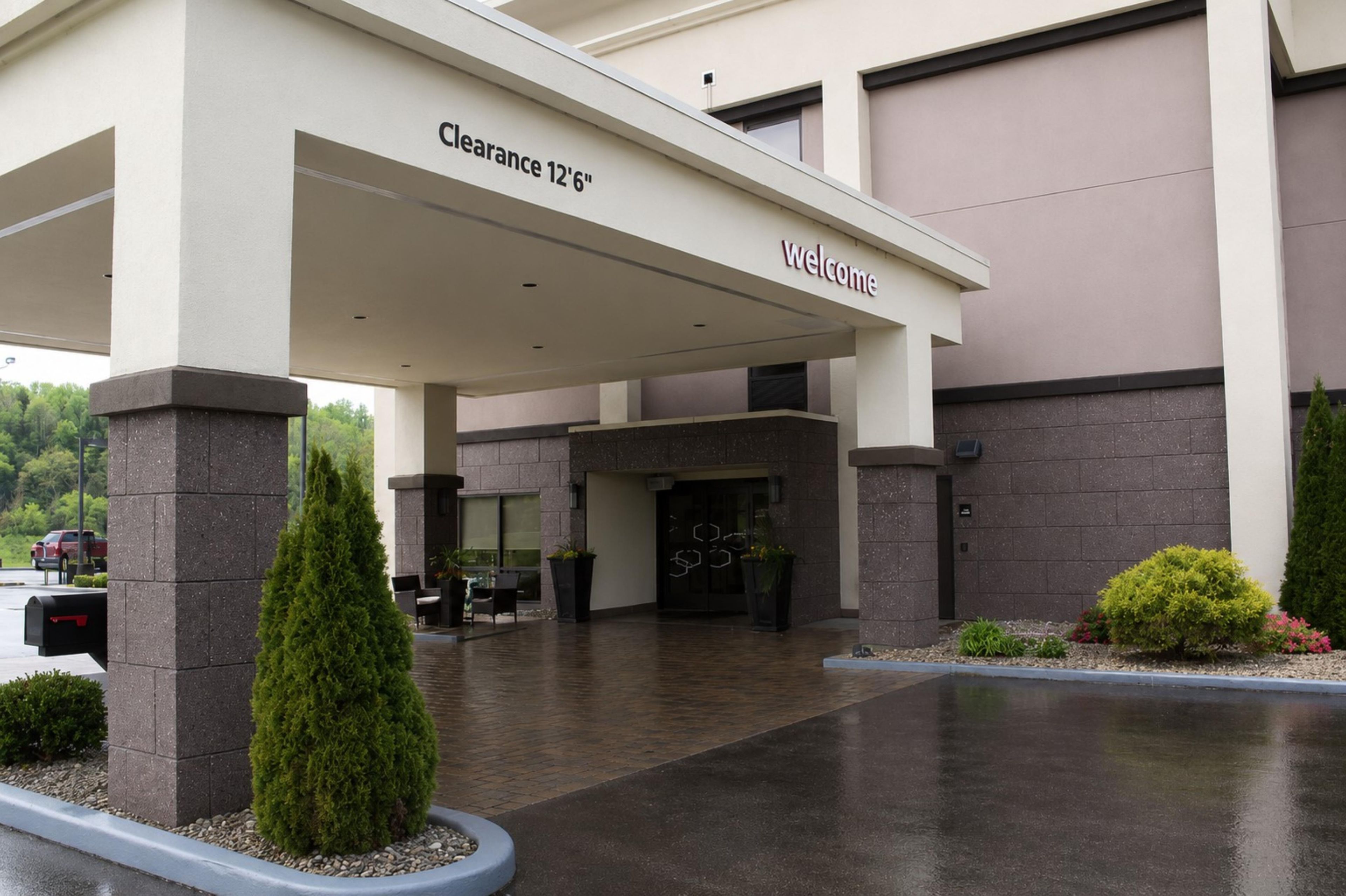 Entrada de hotel con zona cubierta, señalización de 'Clearance 12'6' y un letrero de 'Welcome'.
