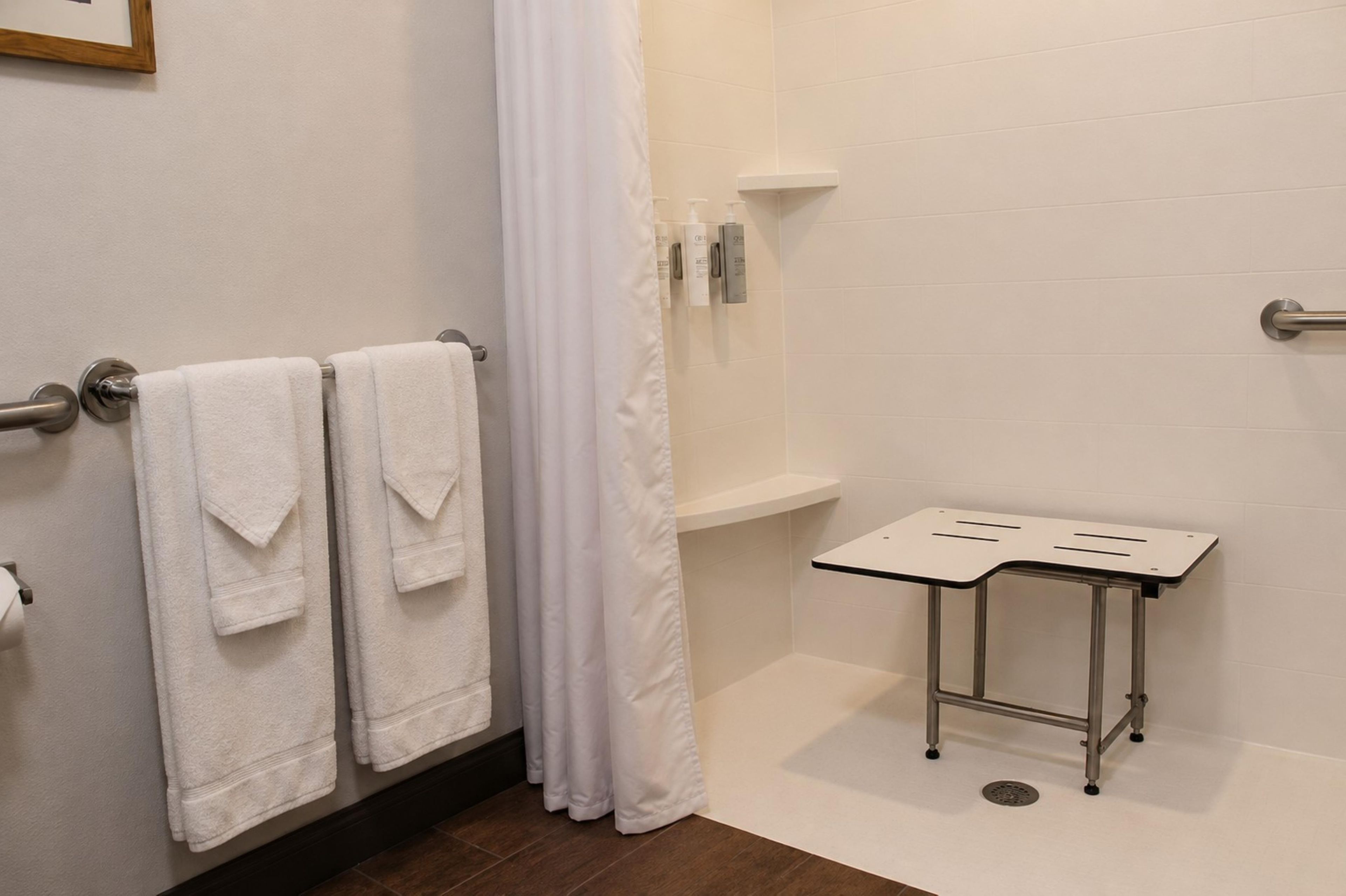 Ein Badezimmer mit zwei Handtüchern an einem Wäscheständer, einer Duschvorhang, einem kleinen Tisch mit Tablett und Pflegeprodukten auf einem Regal.