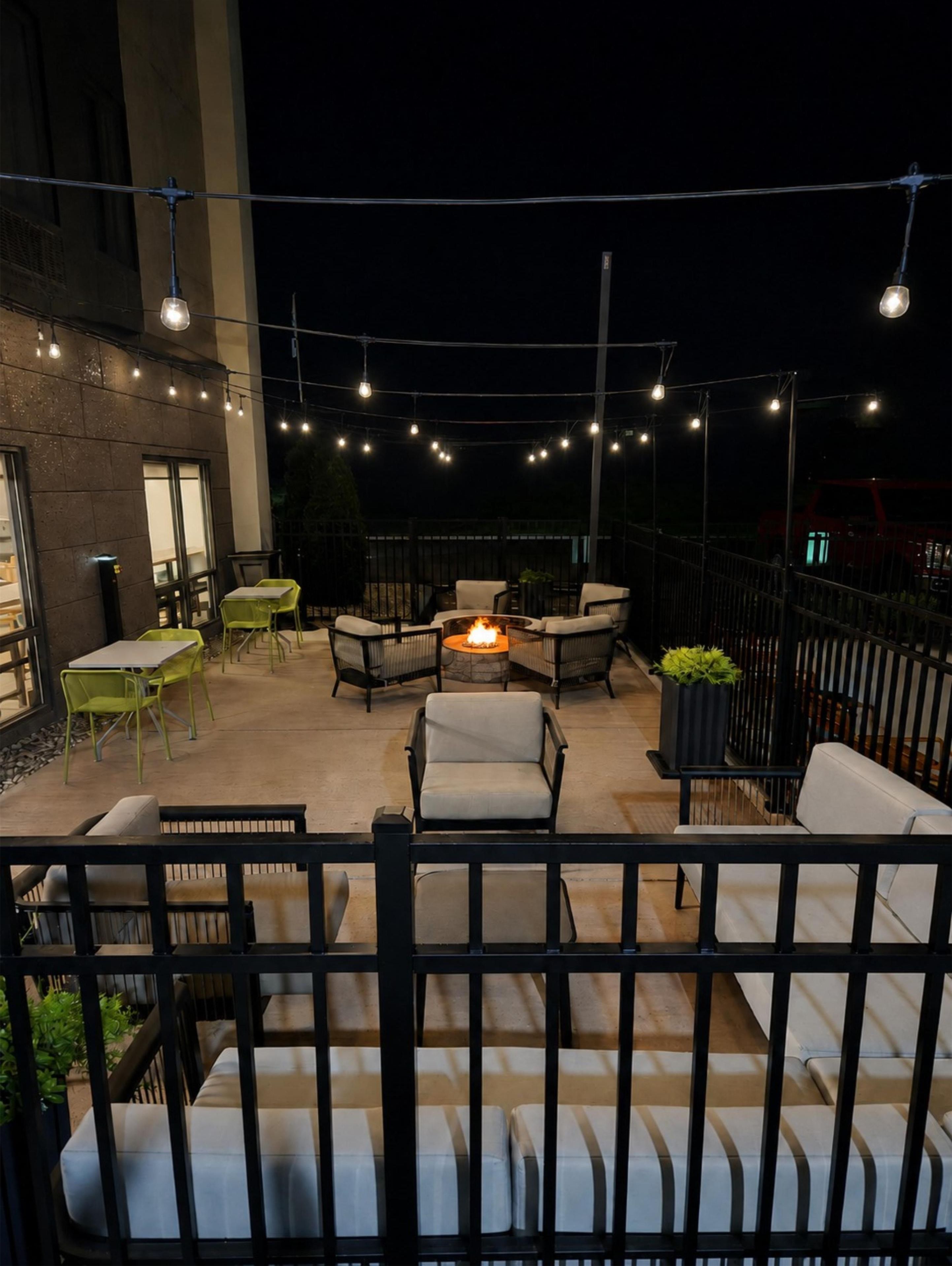 Een terras buiten met zitplaatsen, een vuurkorf en lichtjes.