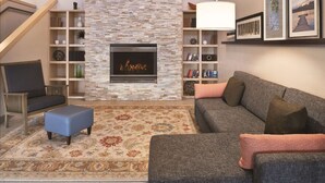 A living room with a fireplace, a sofa, a chair, and a bookshelf. - Country Inn & Suites by Radisson, Germantown, WI (Village of Germantown)