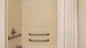 A bathroom with a bathtub, a shower, and a toilet. There are two grab bars installed for safety.