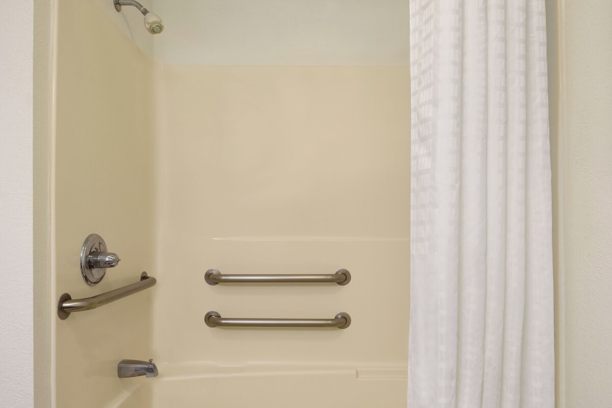 A bathroom with a bathtub, a shower, and a toilet. There are two grab bars installed on the wall for support.