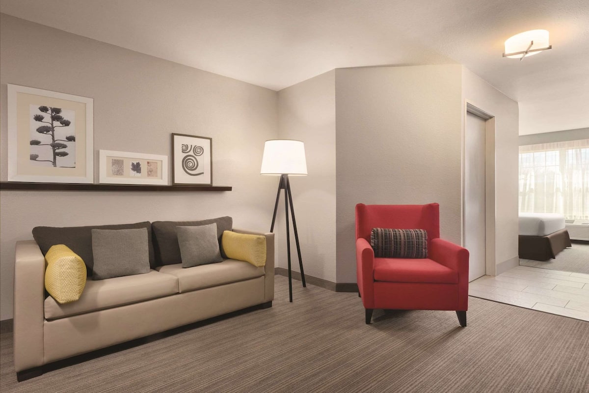 Una sala de estar moderna con un sofá color beige, un sillón rojo, una lámpara de pie y cuadros en la pared.