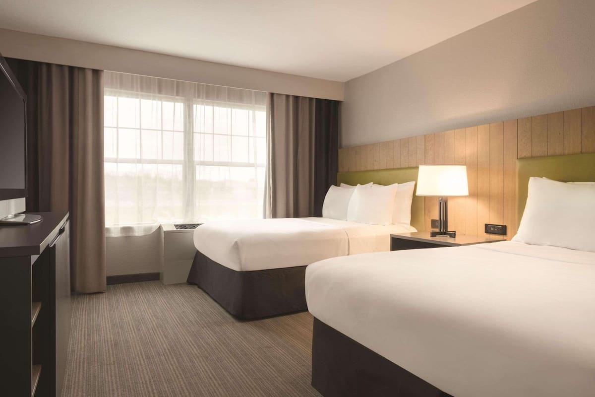 Habitación de hotel con dos camas, un escritorio, una lámpara y una ventana con cortinas.