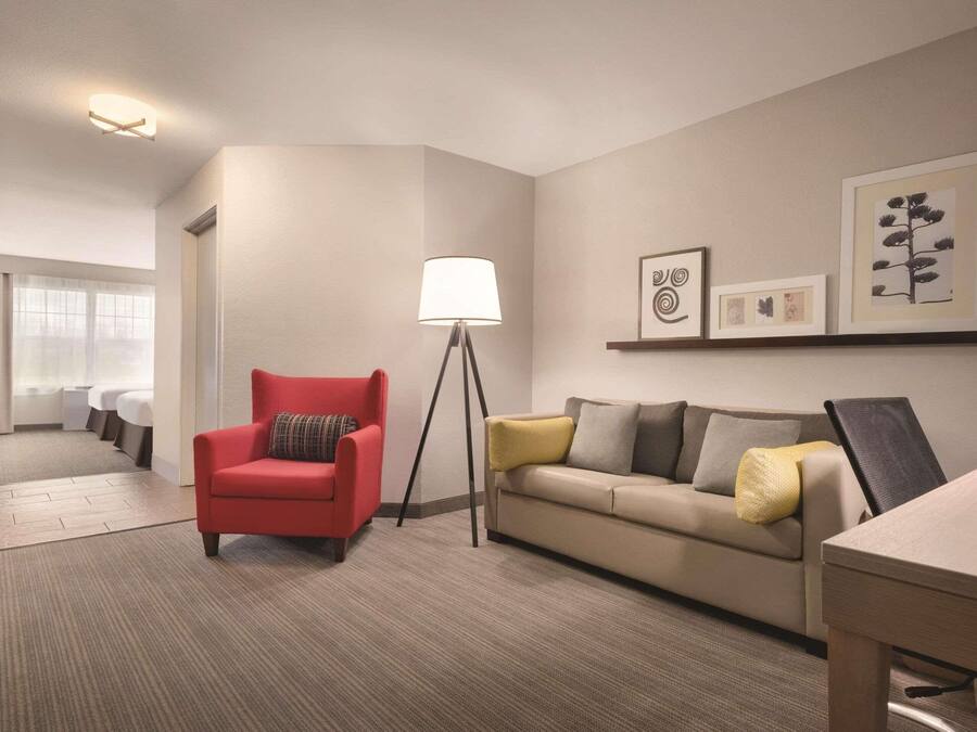 Ett hotellrum med en röd fåtölj, en beige soffa, en golvlampa och inramade konstverk på väggen.