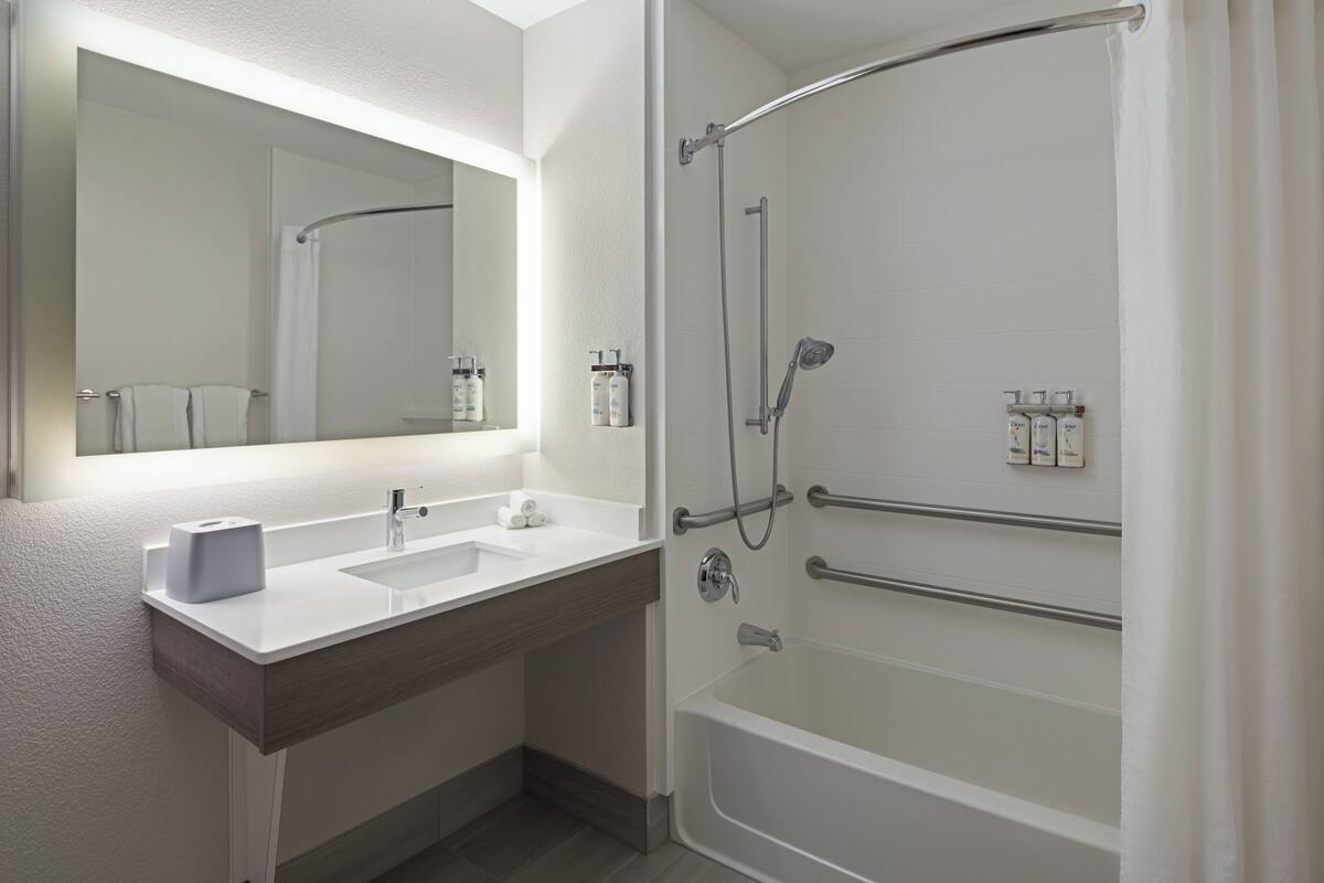 A modern bathroom with a double sink, a large mirror, a shower with a glass door, and toiletries on the wall.
