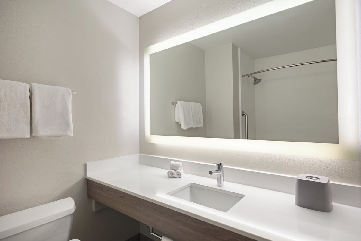 A modern bathroom with a large mirror, a sink, and a toilet.