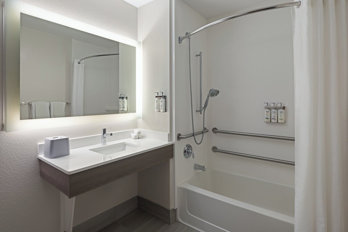 A modern bathroom with a double sink, a large mirror, a shower with a glass door, and toiletries on the wall.