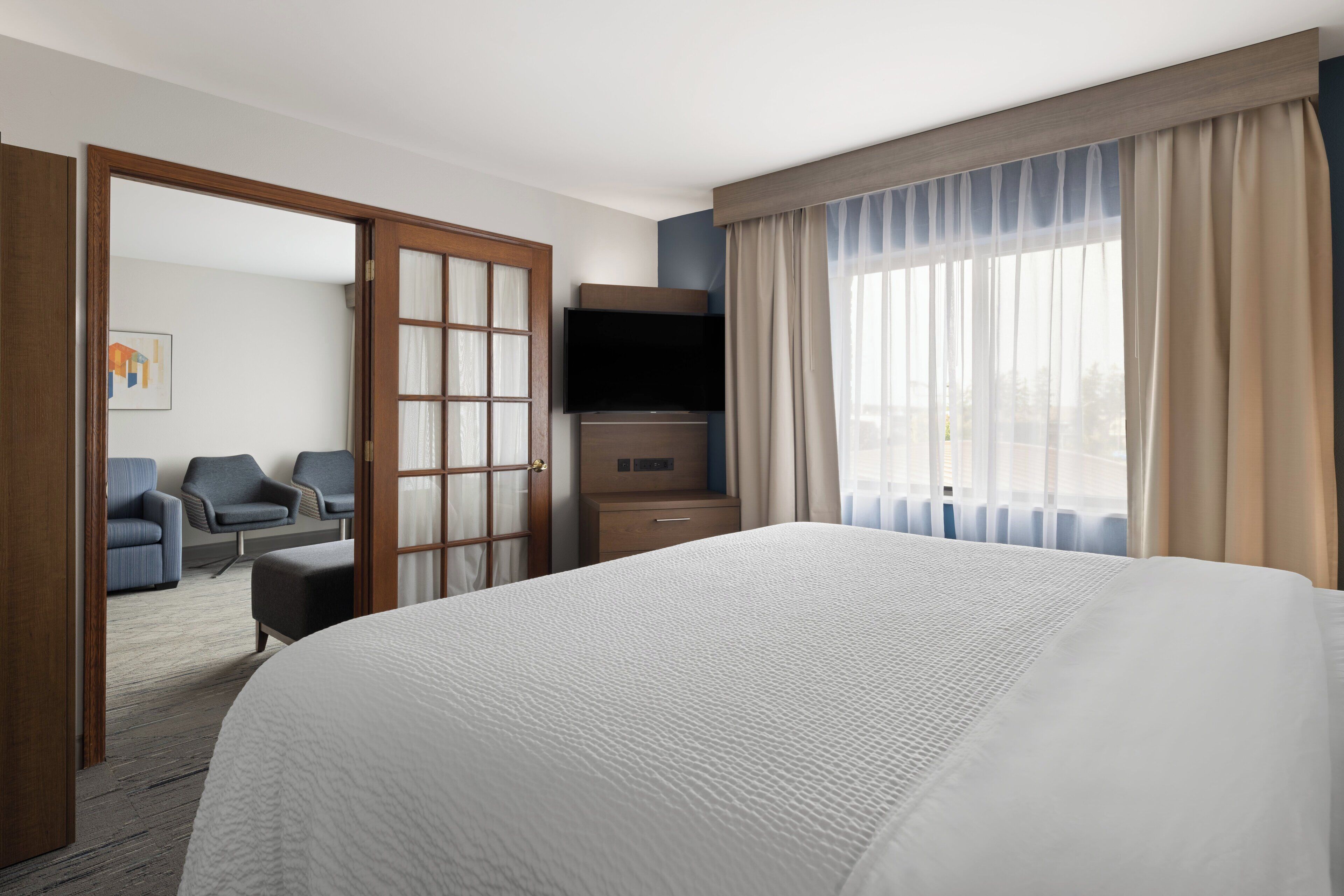Een hotelkamer met een groot bed, een televisie, een bureau en een zithoek met stoelen.