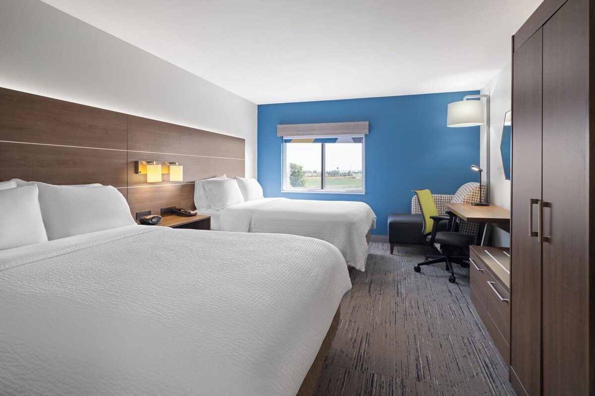 A hotel room with two beds, a desk, a chair, a lamp, and a wardrobe.