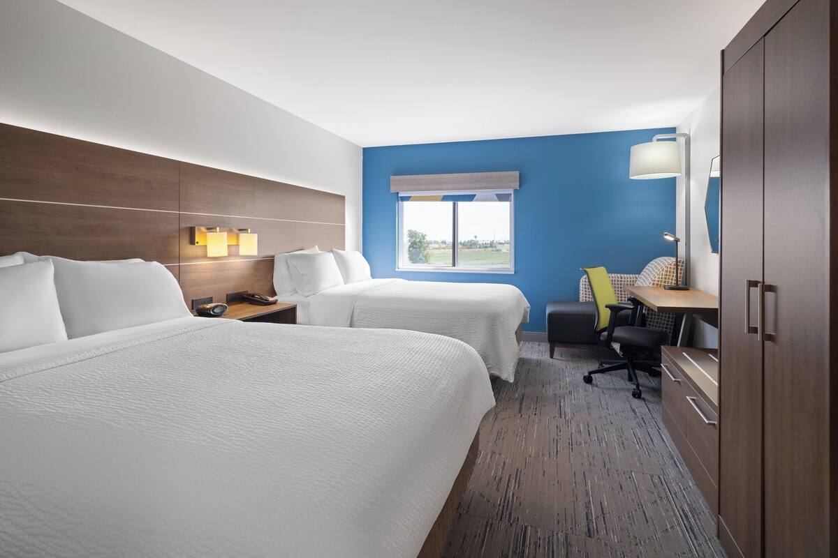 A hotel room with two beds, a desk, a chair, a lamp, and a wardrobe.