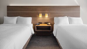 Habitació d'hotel amb dos llits, un capçal de fusta, taules de nit amb làmpades i una petita estantella.