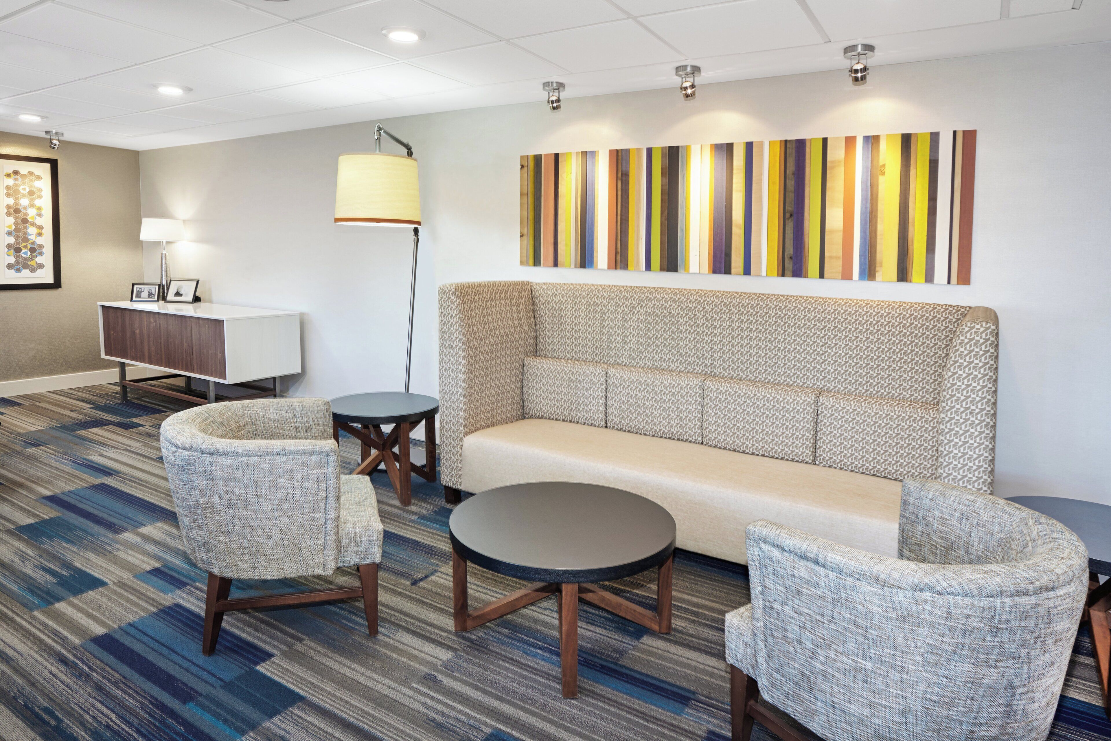 A modern hotel lobby with a sofa, armchairs, a small table, and a lamp.