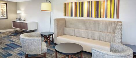 A modern hotel lobby with a sofa, armchairs, a small table, and a lamp.