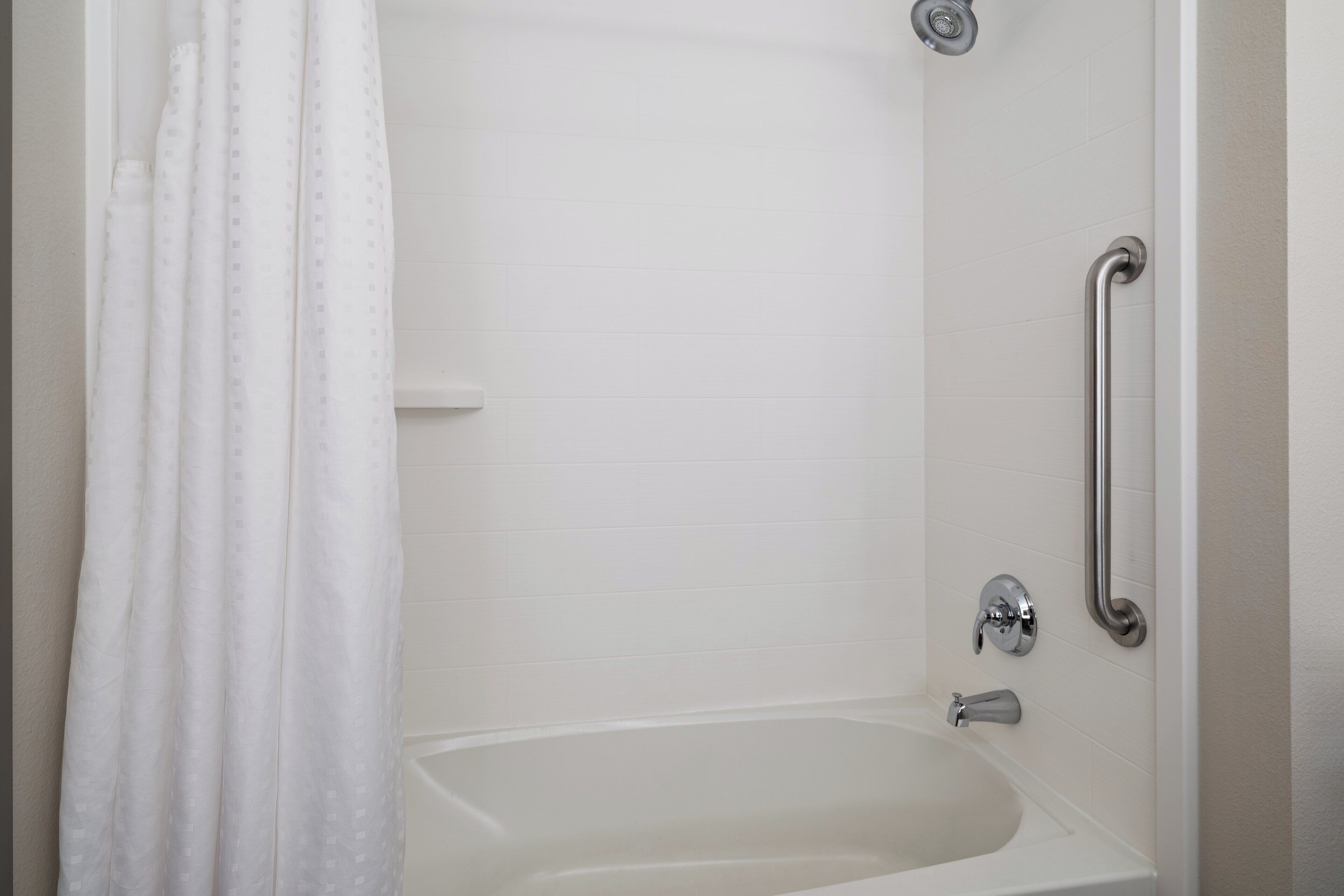 Une baignoire blanche avec un rideau de douche, une barre d’appui et un robinet fixé au mur.