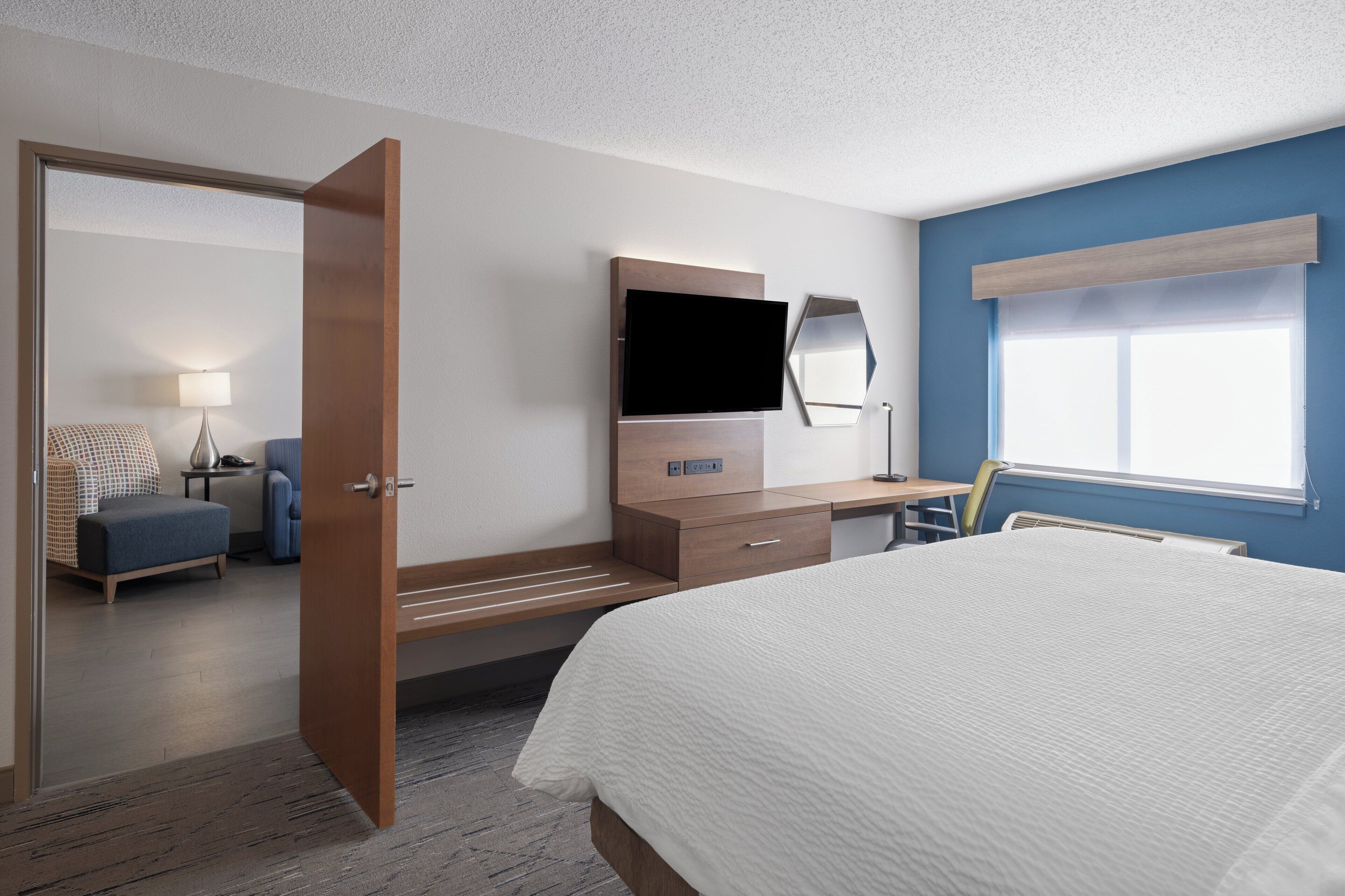 Habitación de hotel con una cama, un escritorio con ordenador, televisor, silla y lámpara.