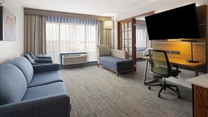 Habitació d'hotel amb un sofà, un escriptori, una cadira, una televisió i una finestra amb cortines.