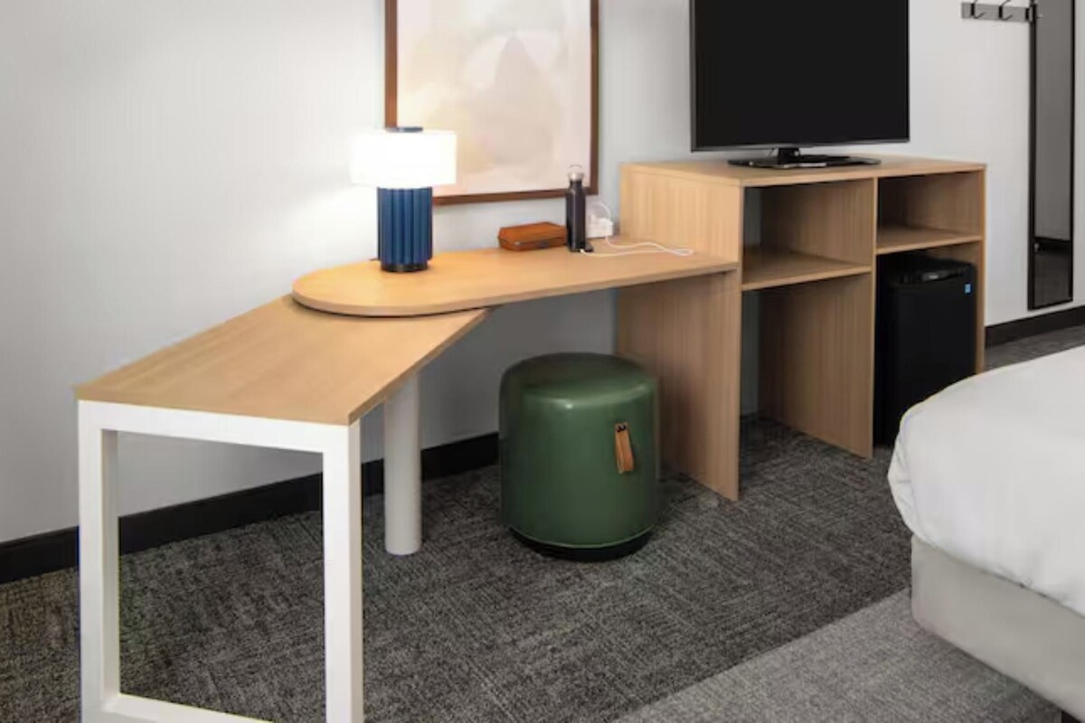Une chambre d’hôtel équipée d’un bureau, d’une poubelle verte, d’un lit et d’un téléviseur.