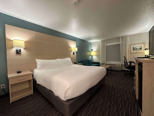 A hotel room with a large bed, bedside tables, a desk, a chair, and two wall-mounted lamps.