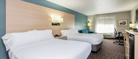 A hotel room with two beds, a desk, a chair, a refrigerator, and a window with curtains.