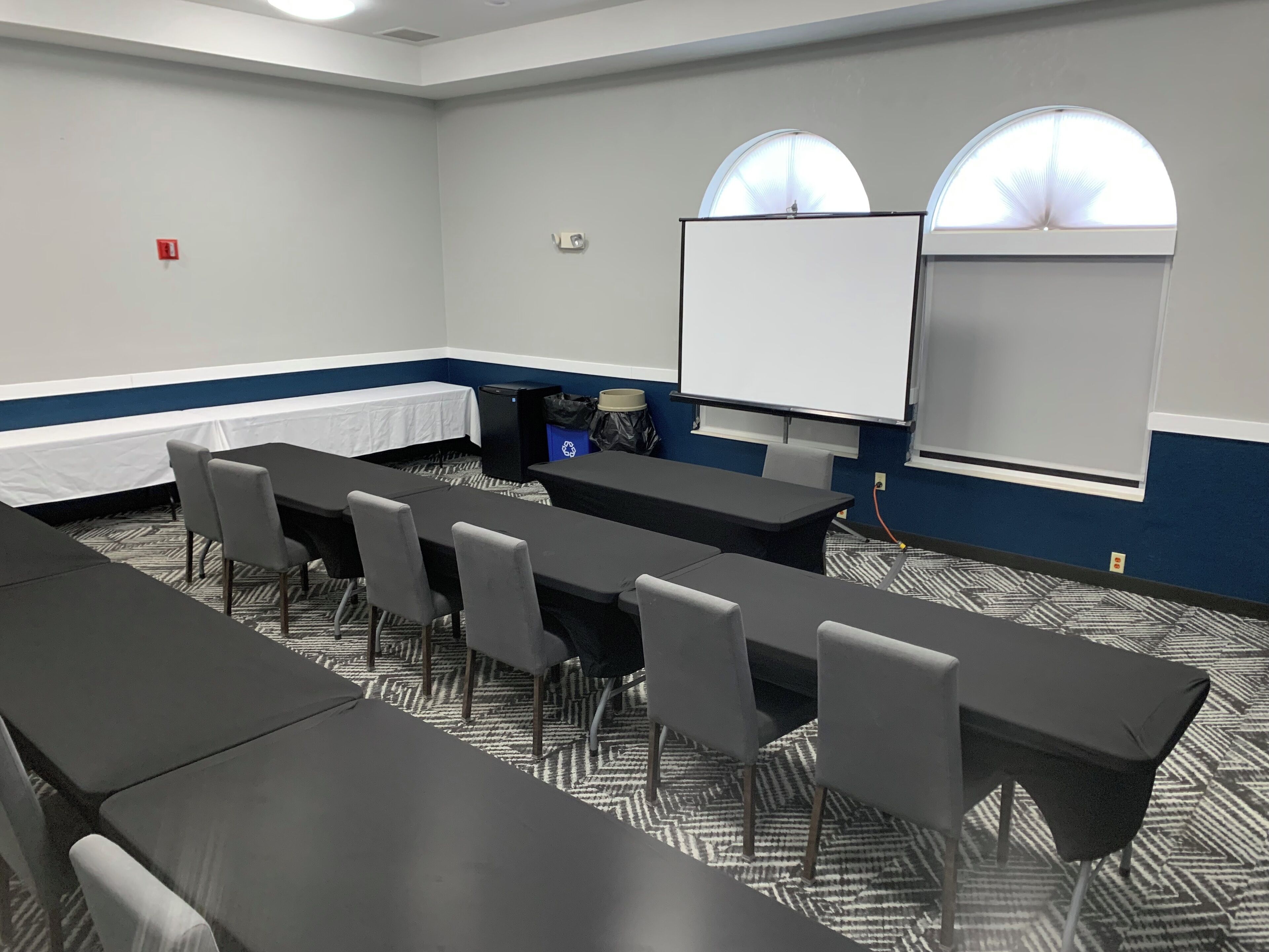 A conference room with a long table, several chairs, a whiteboard, and two arched windows.