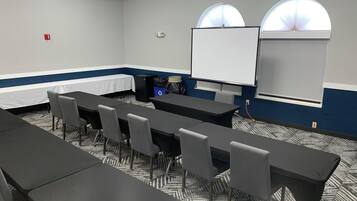 A conference room with a long table, several chairs, a whiteboard, and two arched windows.